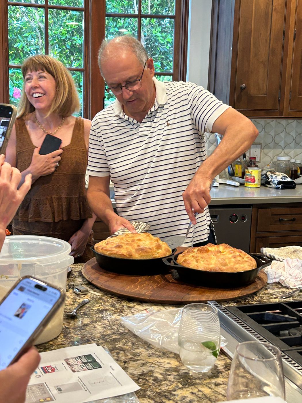 Frank lifting a fresh focaccia from a cast-iron pan while guests watch