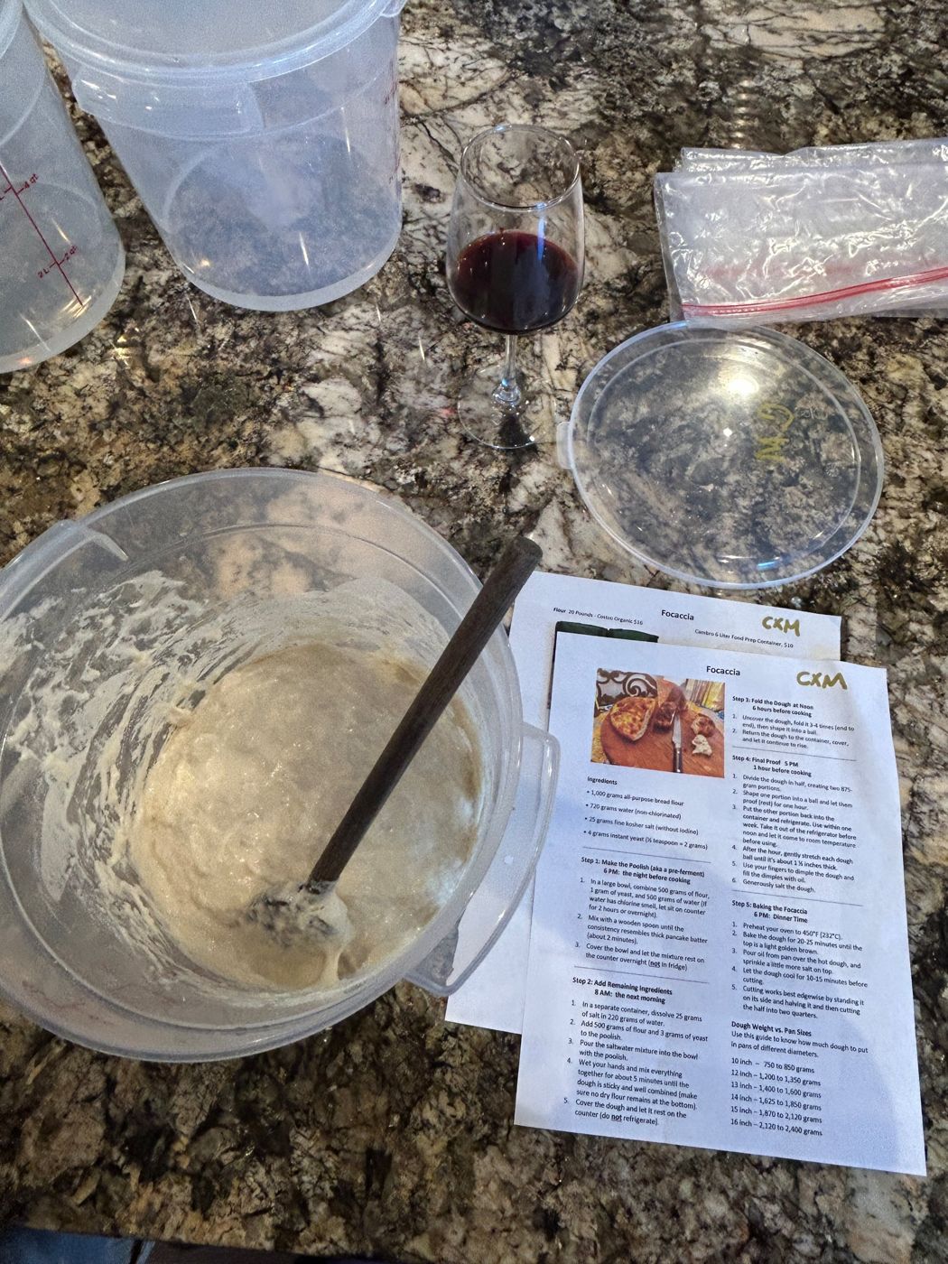 Poolish in a container beside the focaccia recipe handout and a glass of red wine
